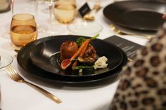 a black plate topped with meat and veggies on top of a white table