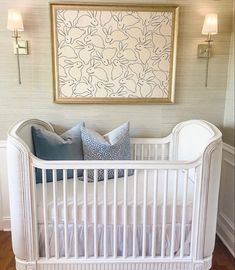 a white crib with blue pillows and a painting on the wall in front of it