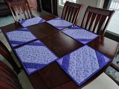 a wooden table topped with purple and blue quilted place mats on top of it