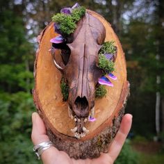 a hand holding a piece of wood with flowers on it and a cow's head