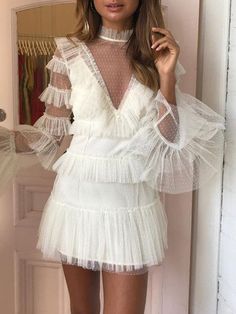 a woman standing in front of a mirror wearing a white dress with sheer shoulders and long sleeves