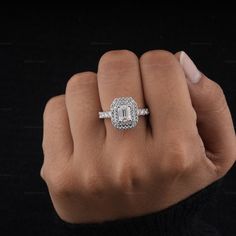 a woman's hand holding an engagement ring with a diamond center and halo setting