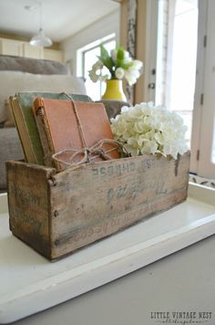 an old wooden box with books and flowers in it sitting on a table next to a couch