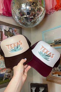 a person holding up two hats with the word texas on them in front of a disco ball