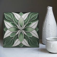 a white vase sitting next to a green and white tile