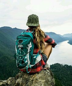 a woman sitting on top of a mountain looking out over the water and mountains in the distance