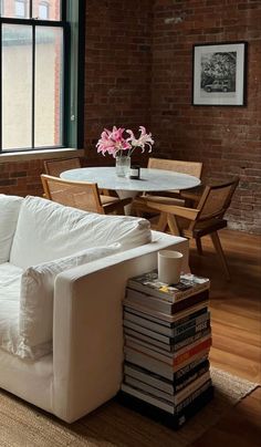 a white couch sitting in front of a window next to a table with books on it