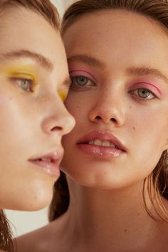 two young women with bright makeup are looking at each other's eyes and make - up