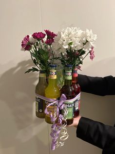 a person holding three beer bottles with flowers in them and tied to the wall behind it