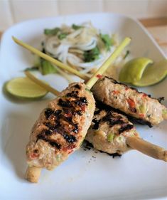 two chicken skewers on a white plate with lime wedges