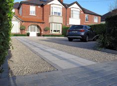 a car is parked in front of a large brick house on a gravel driveway with trees and bushes