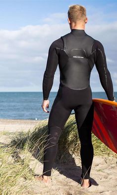 a man in a wet suit holding a surfboard on the beach near the ocean