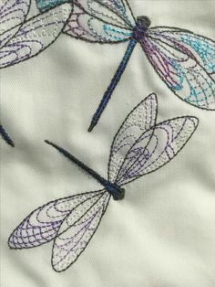 three dragonflys on white fabric with blue and purple threadwork in the middle