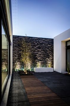 an outdoor area with a wooden walkway and stone wall behind it at night, illuminated by lights