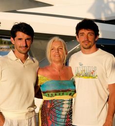 two men and a woman standing next to each other in front of a white boat