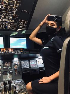 a woman wearing a face mask sits in the cockpit of an airplane and adjusts her visor