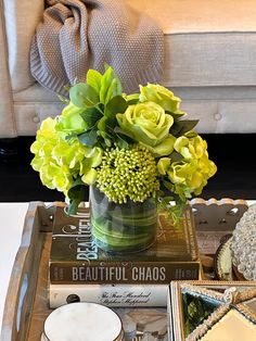 a table topped with books and flowers on top of a wooden tray next to a couch