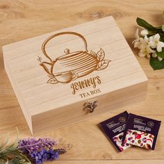 a wooden box with some tea bags and flowers on the table next to it,