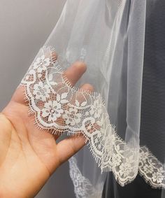 a hand holding a piece of white lace on top of a veil