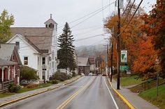 an empty street with houses on both sides and trees in the background, during autumn