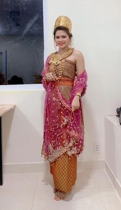 a woman standing in front of a window wearing a pink and gold dress with an elaborate head piece