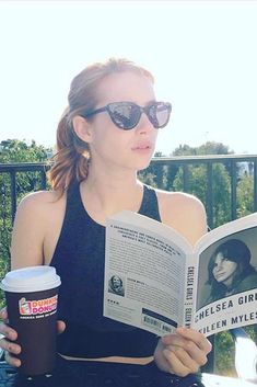 a woman sitting at a table reading a book and holding a coffee in her hand