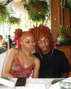 two people sitting at a table with plants in the background