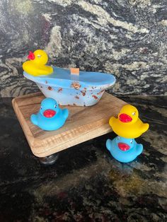 two rubber ducks sitting in front of a blue bath tub on a wooden board with a marble wall behind it