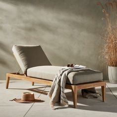 a chaise lounge chair sitting on top of a tile floor next to a potted plant