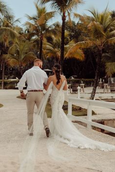 a bride and groom walking on the beach in front of palm trees at their wedding