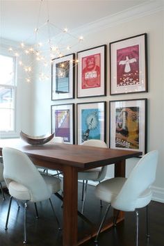 a dining room table with chairs and pictures on the wall above it, along with hanging lights