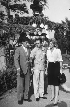 black and white photograph of three people standing in front of an outdoor market with many items on display