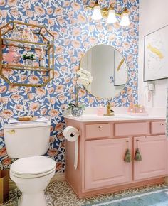 a bathroom with pink and blue wallpaper, gold mirror, white toilet and sink