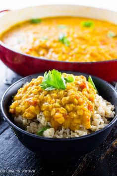 two bowls filled with rice and curry on top of a wooden table next to a red pan