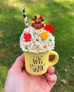 a hand holding a yellow cup filled with whipped cream and toppings that says give thanks