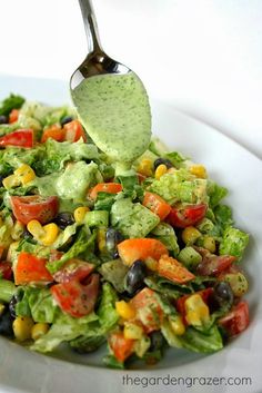 a salad with dressing being drizzled over it on a white plate next to a spoon