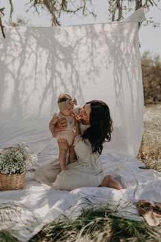 a woman sitting on top of a blanket holding a baby