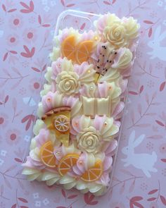 a cell phone case with some fruit and flowers on the front, sitting on a pink floral background