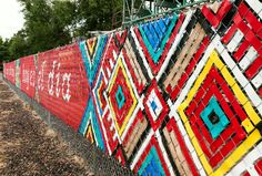 the fence is covered with colorful quilts on it's sides, and there are trees in the background