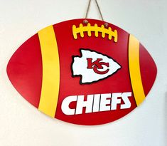 a kansas chiefs football shaped sign hangs on the wall next to a white wall with a red and yellow stripe