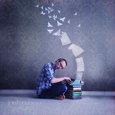 a man sitting on the floor next to a stack of books with paper birds coming out of it