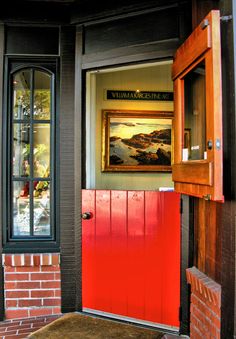 a red door is open on the outside of a brick building with a painting hanging above it