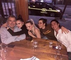 a group of people sitting at a table with wine glasses in front of them, posing for the camera