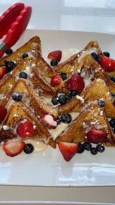 french toast with strawberries and blueberries on a white plate next to a red spatula