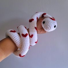 a hand is holding a crocheted snake with hearts on it's tail