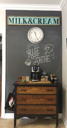 there is a chalkboard on the wall above a dresser with a clock and coffee maker