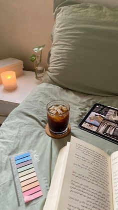 an open book sitting on top of a bed next to a cup of coffee and a candle