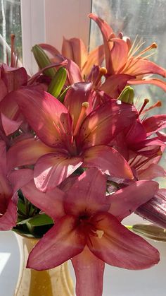 a yellow vase filled with pink flowers next to a window