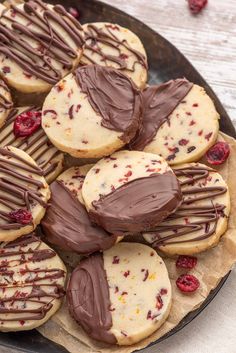 a plate full of cookies with chocolate drizzled on them and raspberries