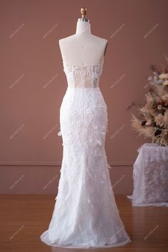 a white wedding dress on display in front of a pink wall and table with flowers